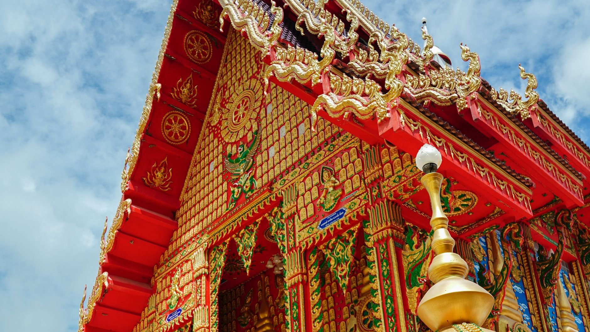 An ornate gold and red Thai Buddhist temple hall against a blue sky (illustrative stock photo)